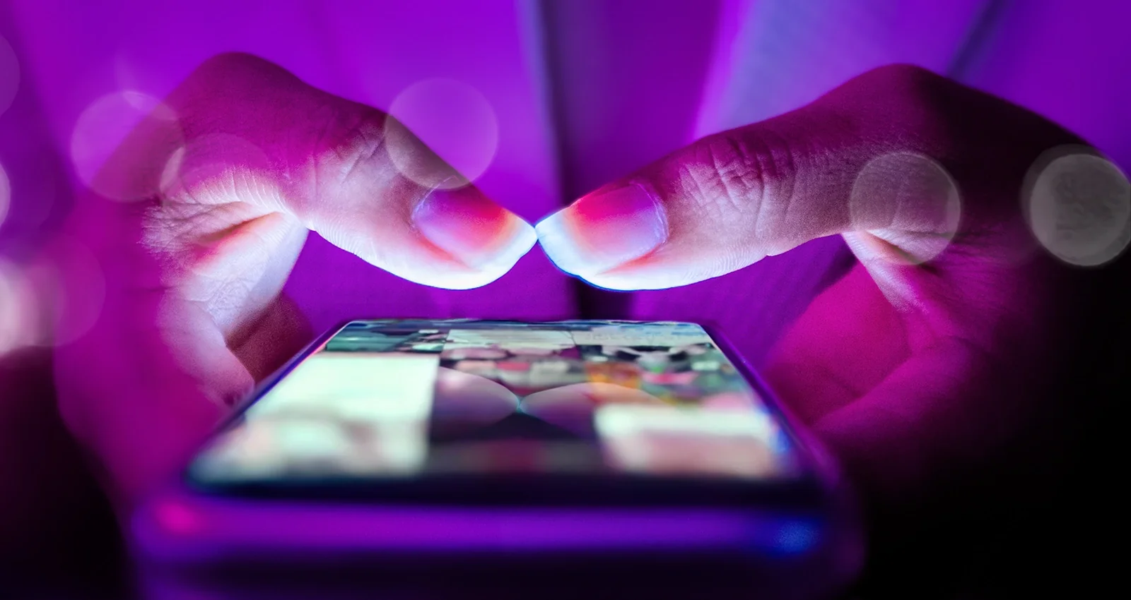 Close-up of hands holding a smartphone lit by purple light